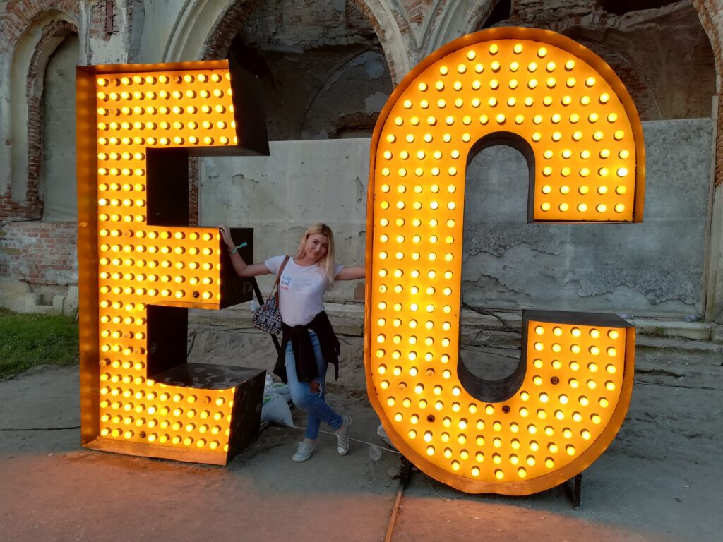 Girl standing in between the huge letters E and C that stand for Electric Castle festival